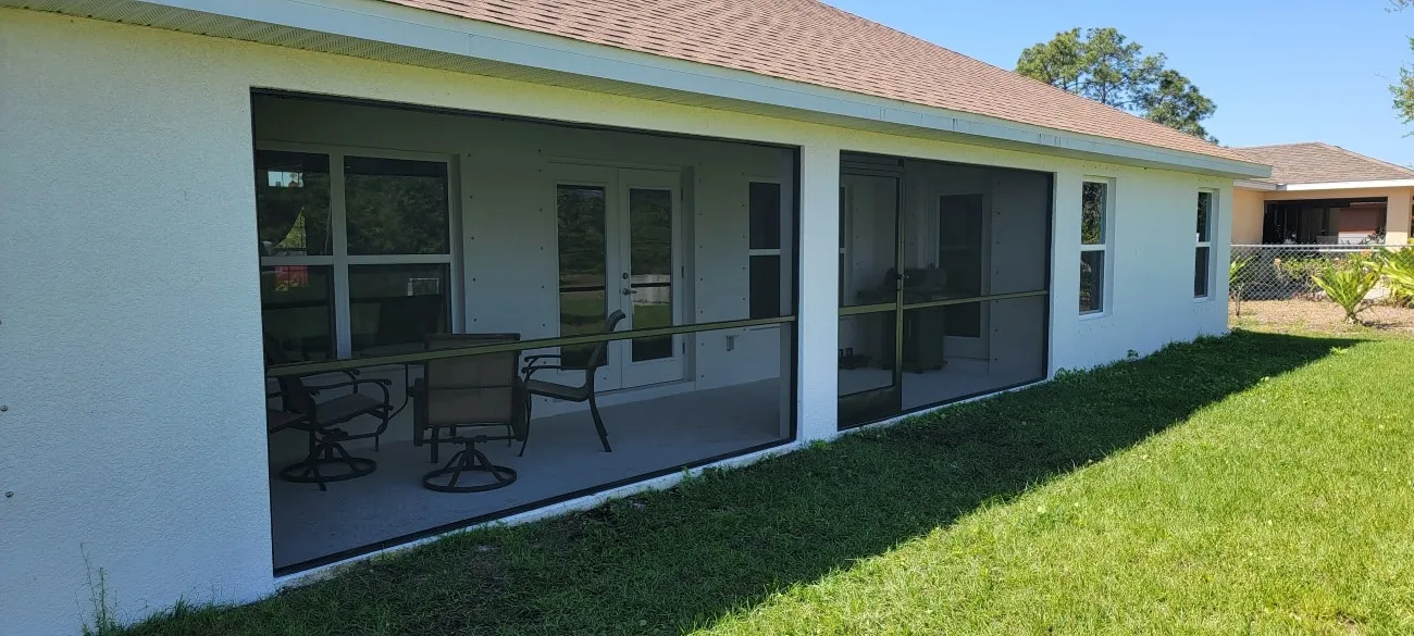 Screened lanai with patio furniture on the back of a white Florida home under a clear blue sky