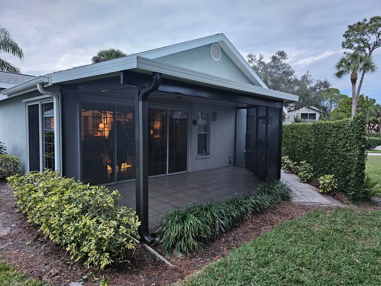 Screened lanai with dark aluminum soffit, gutter and downspout on a Florida home at dusk