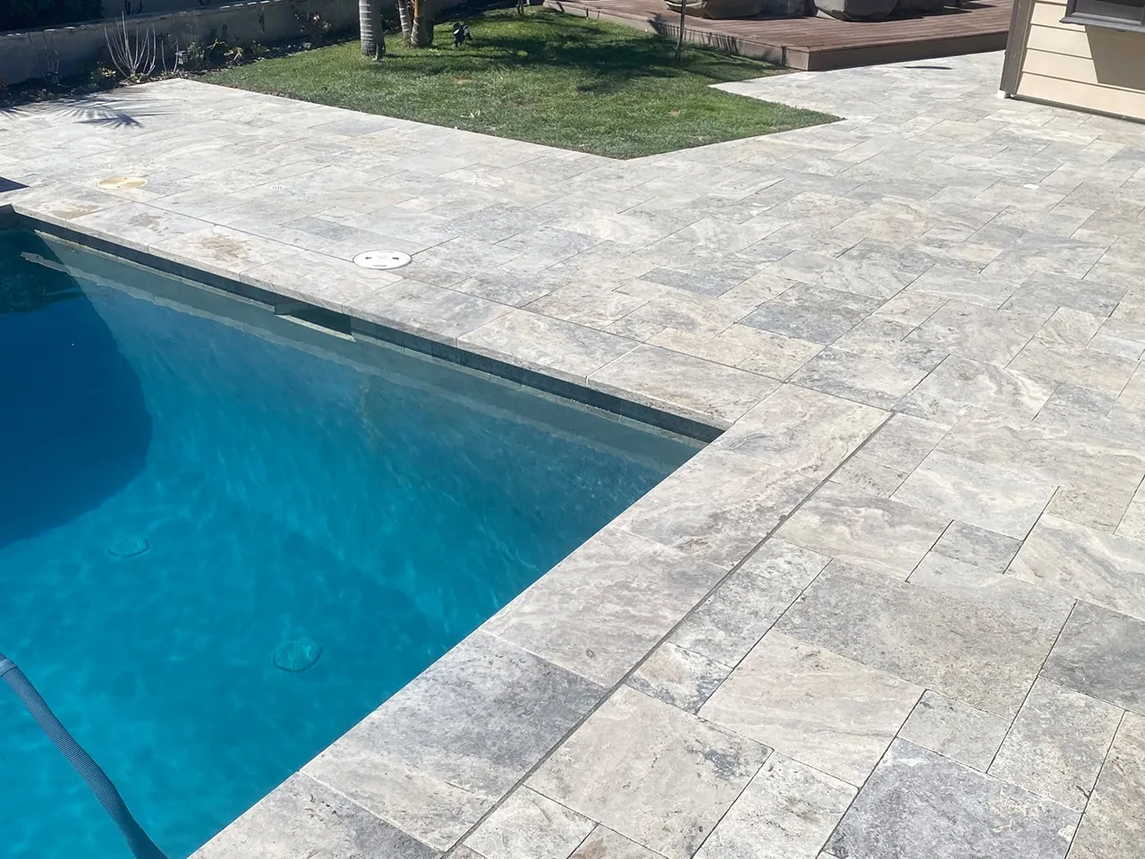 Silver travertine paver pool deck with matching coping beside a backyard lawn