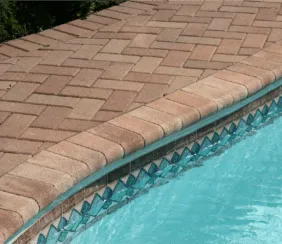 Tan brick pavers in a herringbone pattern with bullnose coping along a pool edge