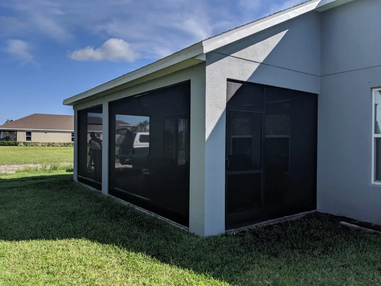 New screen enclosure with dark mesh panels and screen door on a light gray Florida home