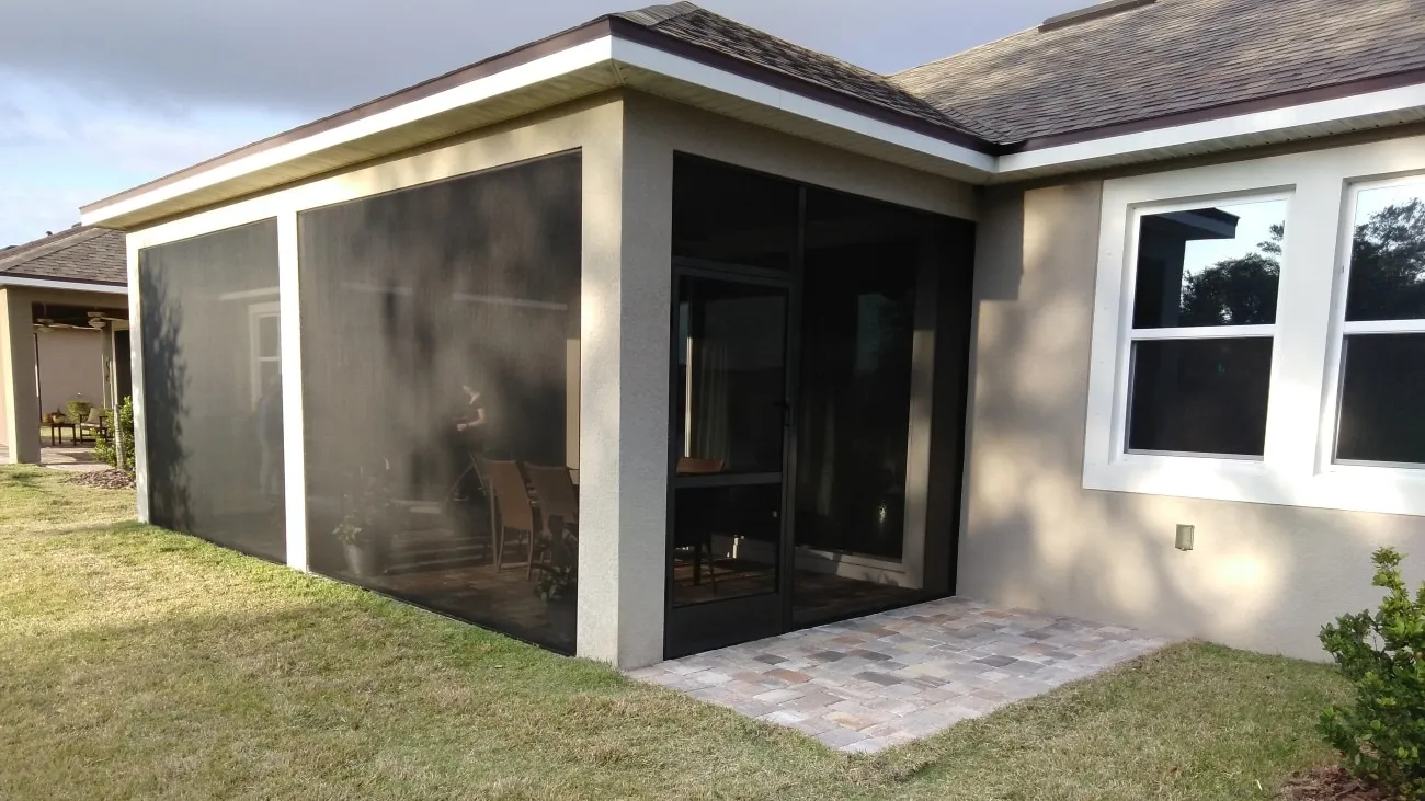 Screened patio with aluminum-frame door on a beige Florida home, dining chairs visible behind the mesh