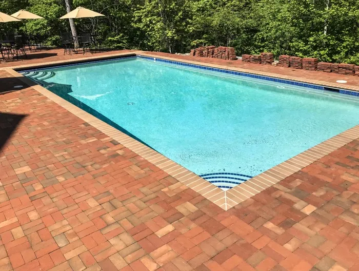 Red brick paver deck surrounding a rectangular pool with blue waterline tile