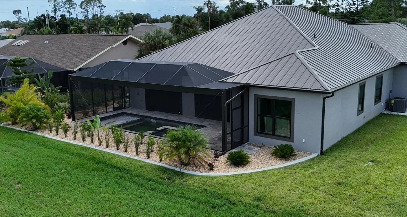 Aerial view of a bronze clear view pool cage attached to a metal-roof Florida home with fresh landscaping