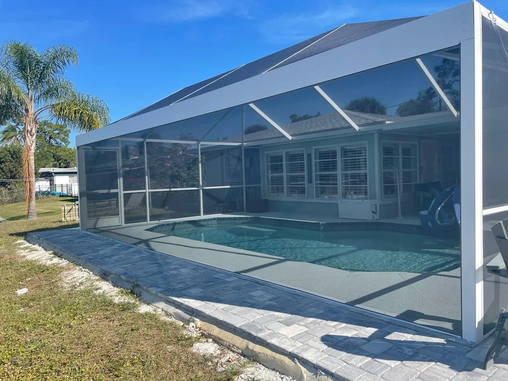 White-frame clear view pool cage enclosing a backyard pool in Sarasota with a paver border and palm tree