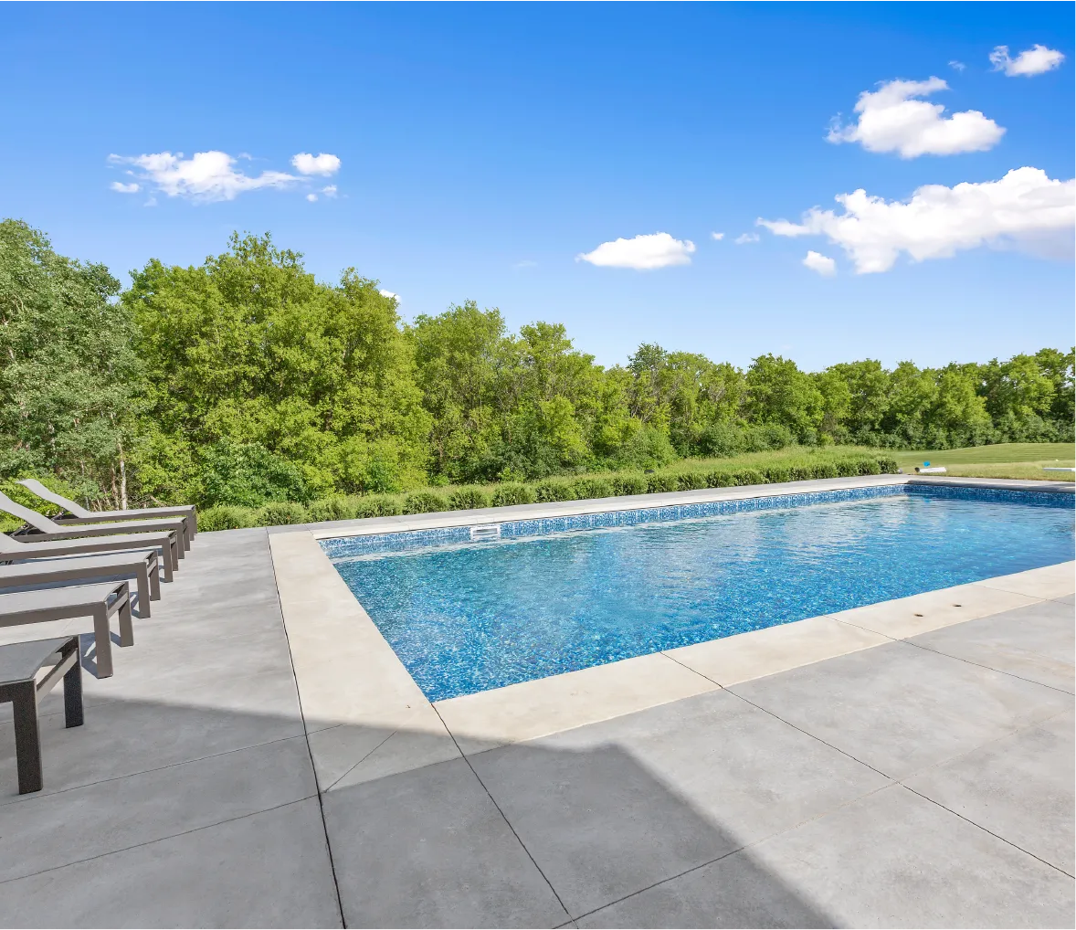 Large-format gray concrete pavers surrounding a rectangular pool with lounge chairs