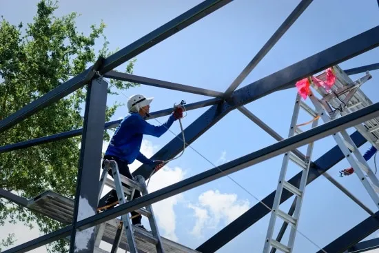 Painter on a ladder applying coating to the upper trusses of a pool cage frame