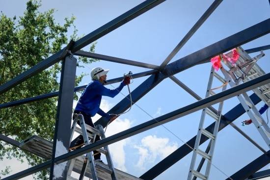 Painter on a ladder spray-coating the aluminum frame of a pool cage in Sarasota, Florida