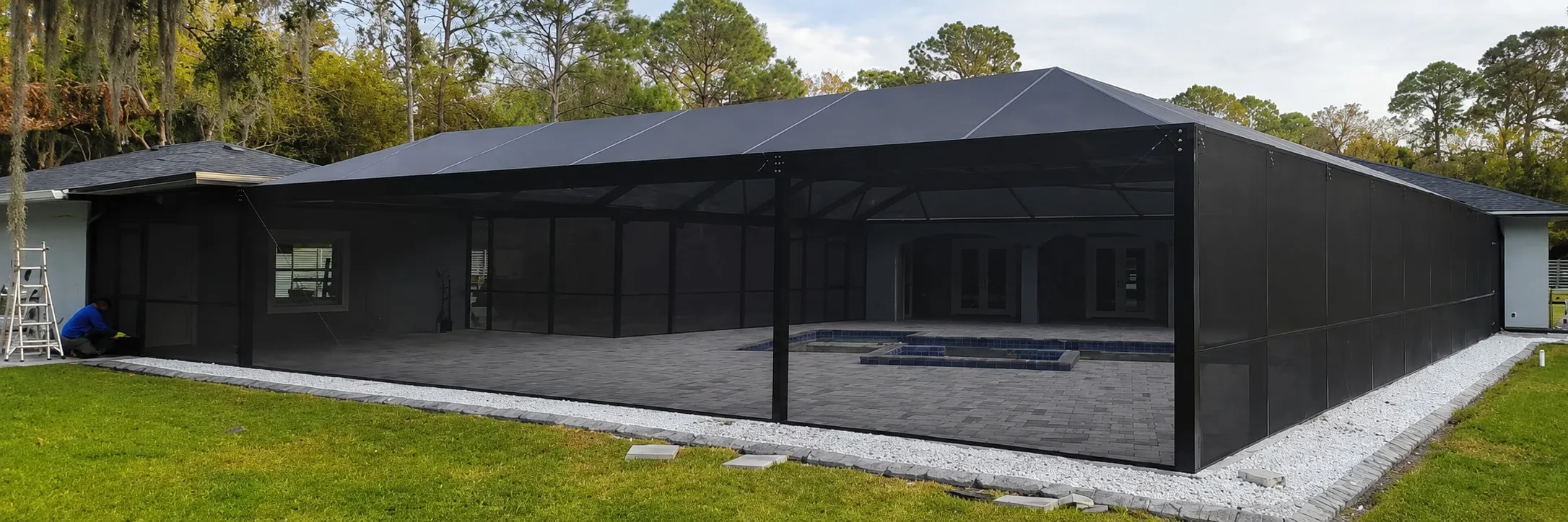 Finished gable-roof pool enclosure with dark privacy screen walls around a paver pool deck