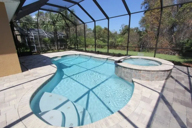 Free-form pool and raised stone spa with a fountain inside a screened lanai enclosure