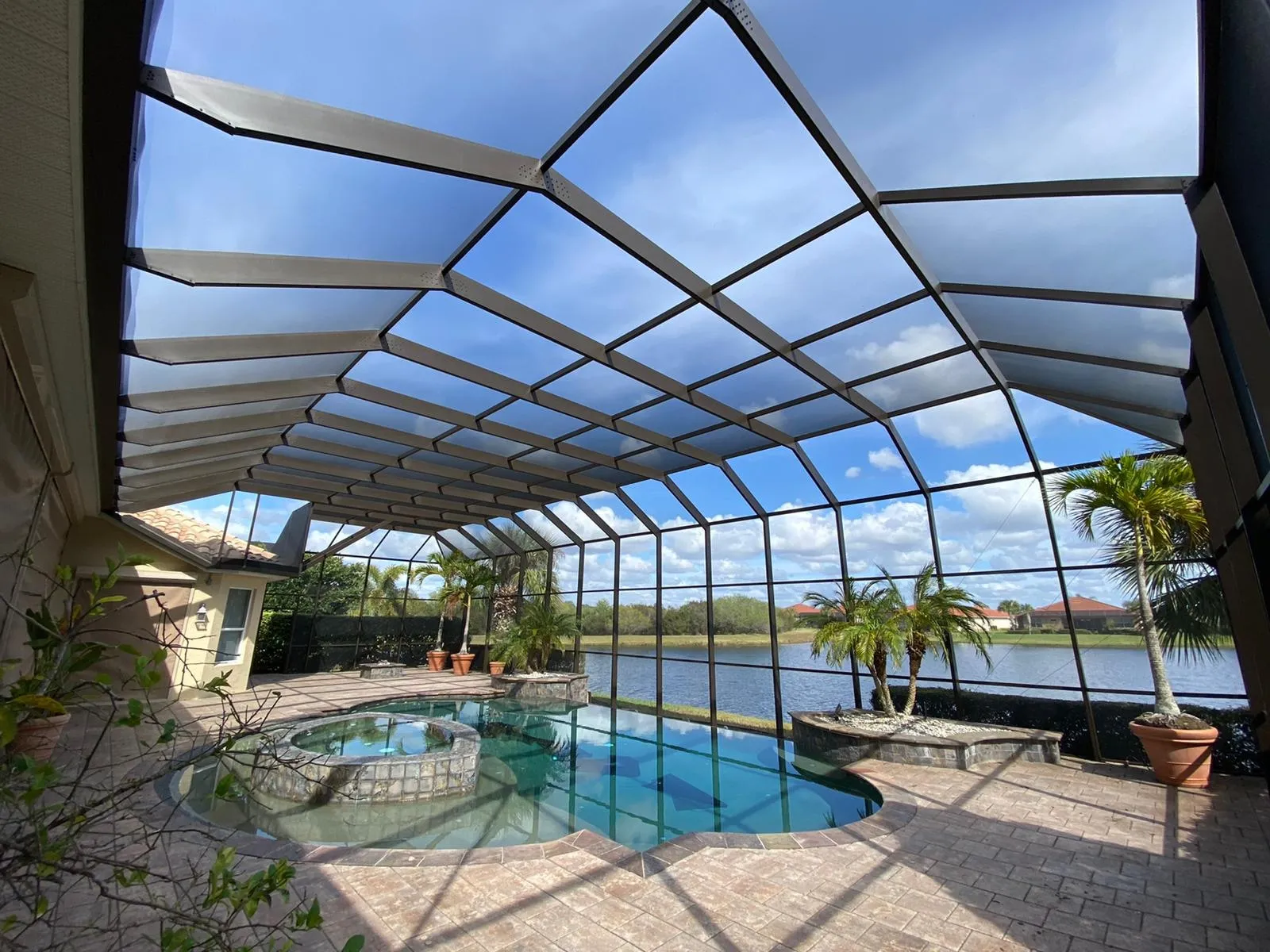 Gable-roof screen enclosure seen from inside, its aluminum ribs rising to the ridge over a pool and spa on the water