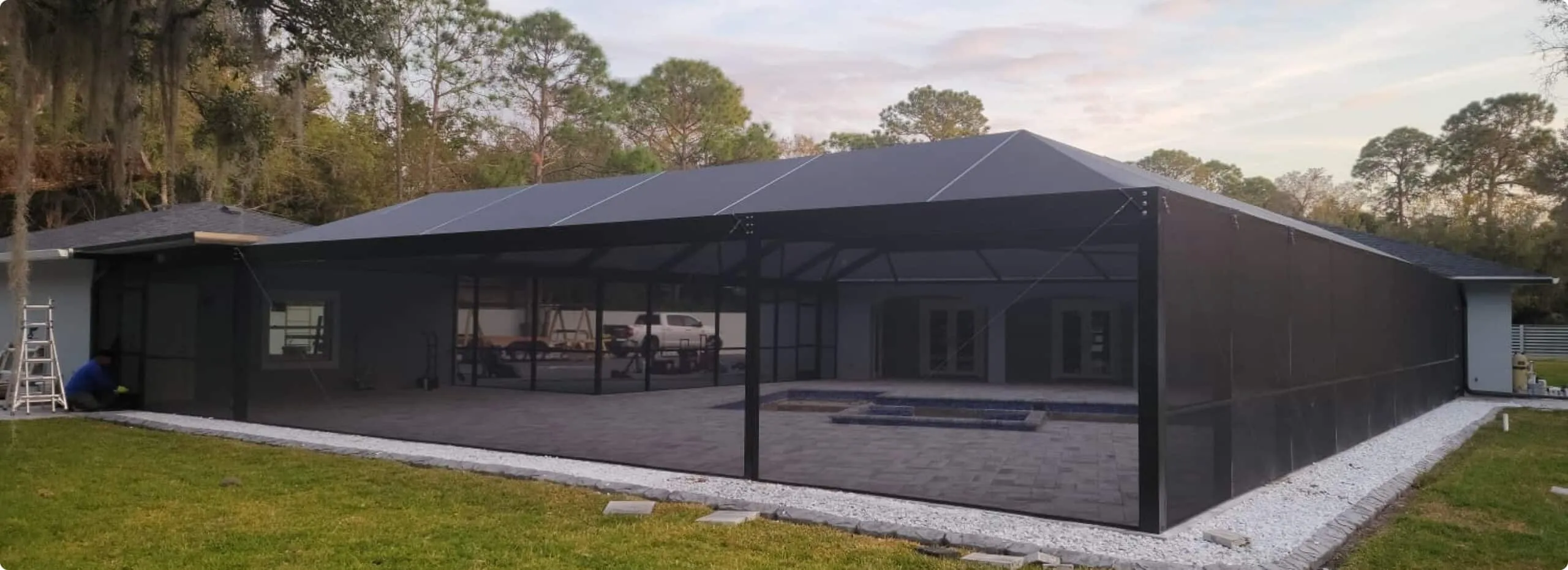Finished gable-roof pool enclosure with charcoal screen mesh at dusk