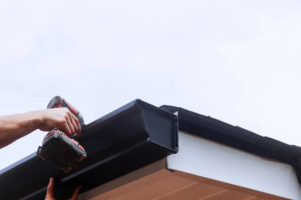 Installer screwing a black seamless gutter to the roof edge at the gable end
