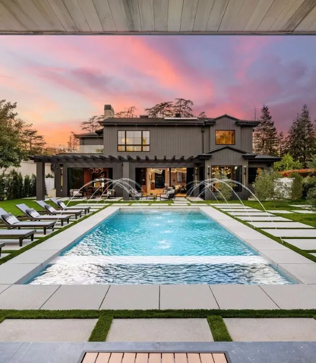 Modern custom pool by pool builders in sarasota fl with water features, spa and travertine pavers at sunset.