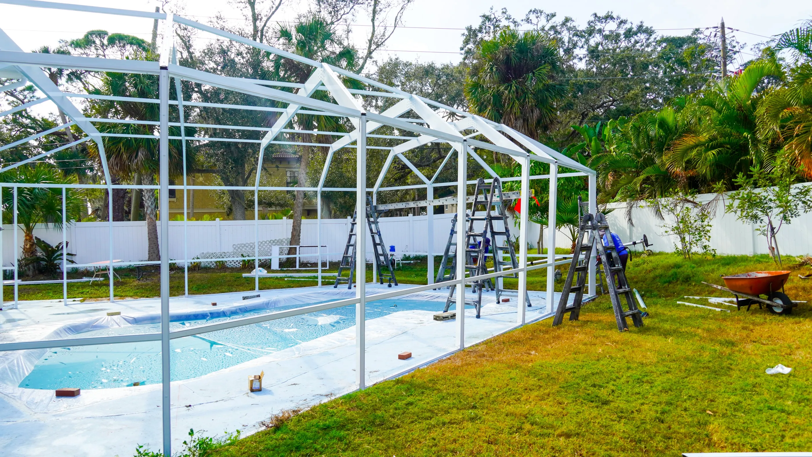 Newly erected white aluminum pool cage frame over a screened Florida pool, before the mesh panels go in