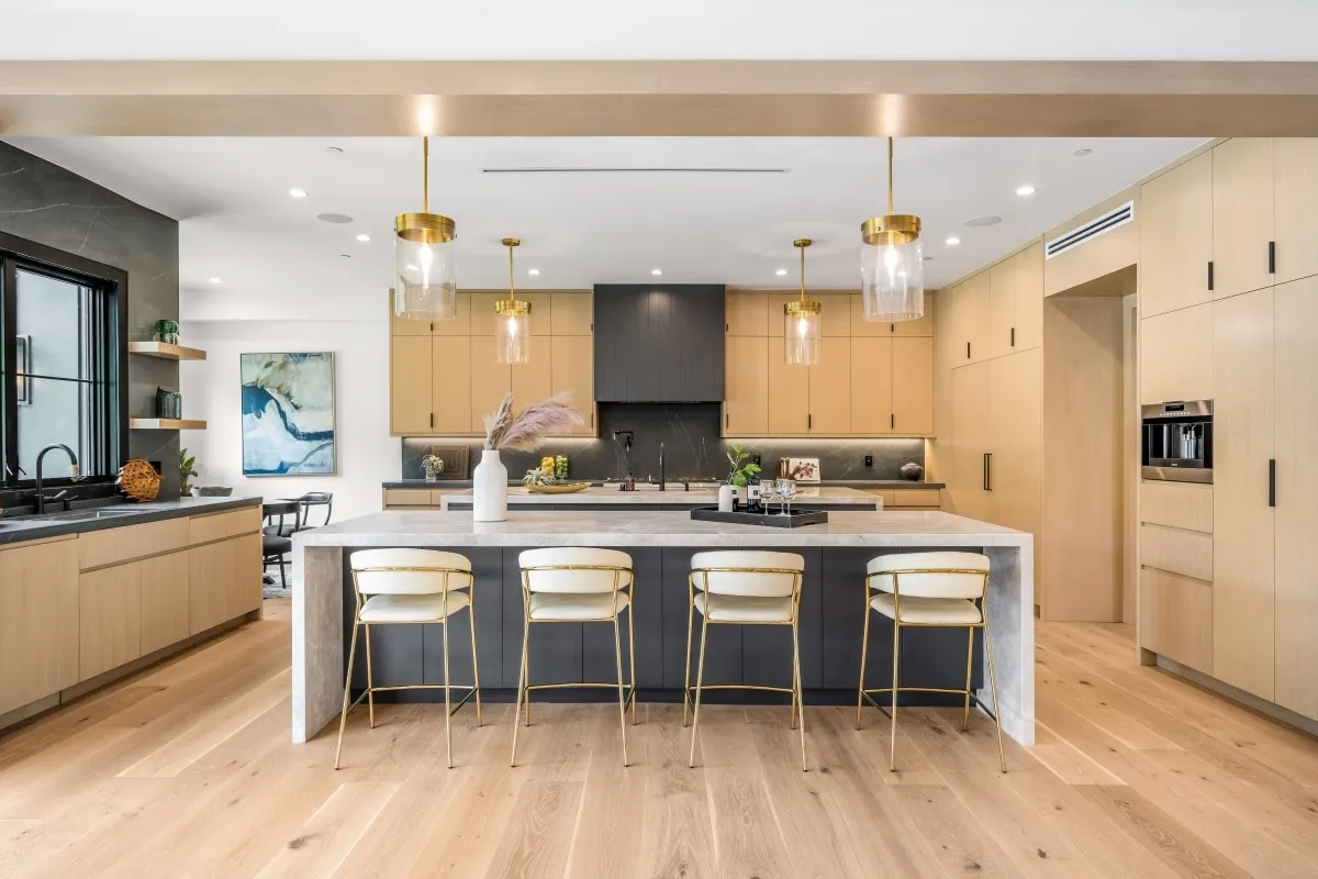 Open kitchen with long stone island, four cream bar stools, and brass pendants