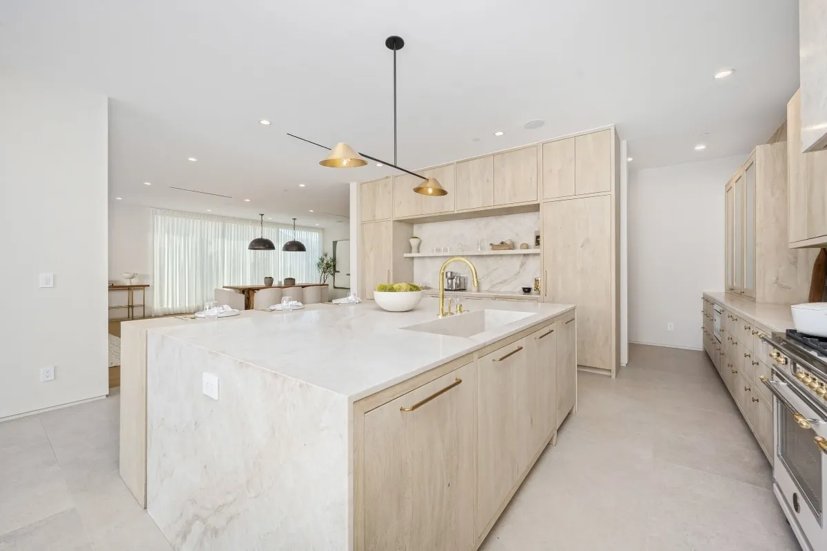 Cream-toned kitchen remodel with oversized marble island and brass faucet