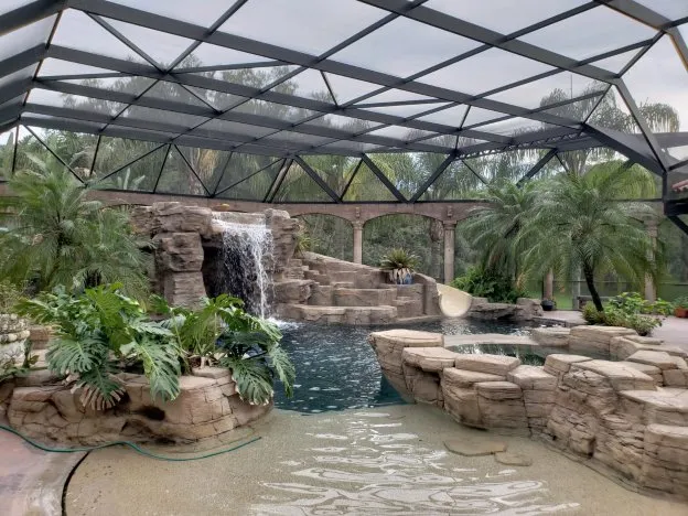 Lagoon-style pool with a rock waterfall grotto under a screen enclosure in Sarasota