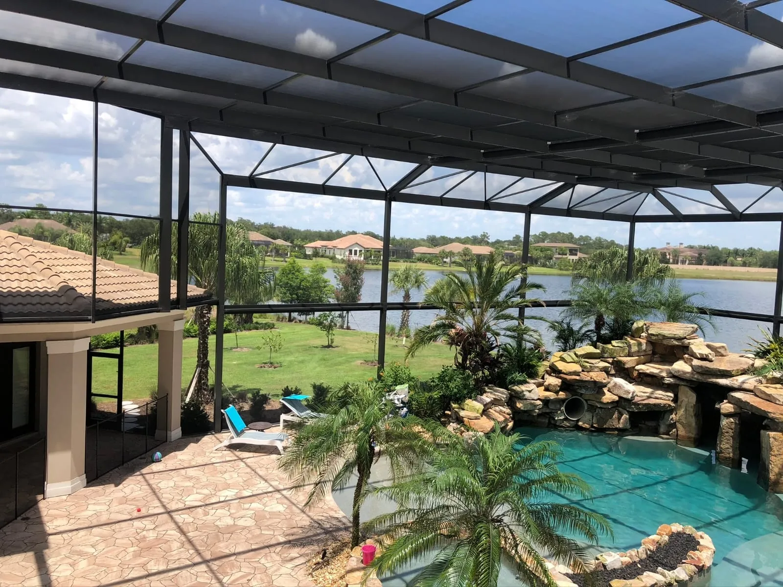 Restored pool cage in dark bronze aluminum seen from inside, over a rock waterfall pool with the lake beyond