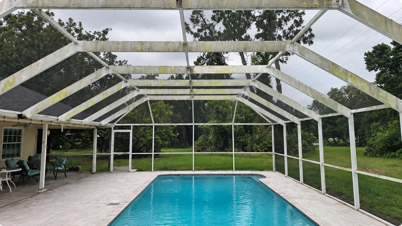 Pool cage before restoration: the aluminum frame oxidized and streaked with mold and algae over the pool deck