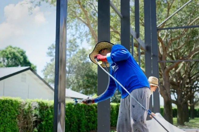 Painter spray-coating a pool cage aluminum frame with an airless sprayer