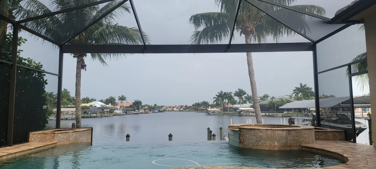 Screened lanai with spa and infinity-edge pool framing a canal view with palms and boat docks in Sarasota