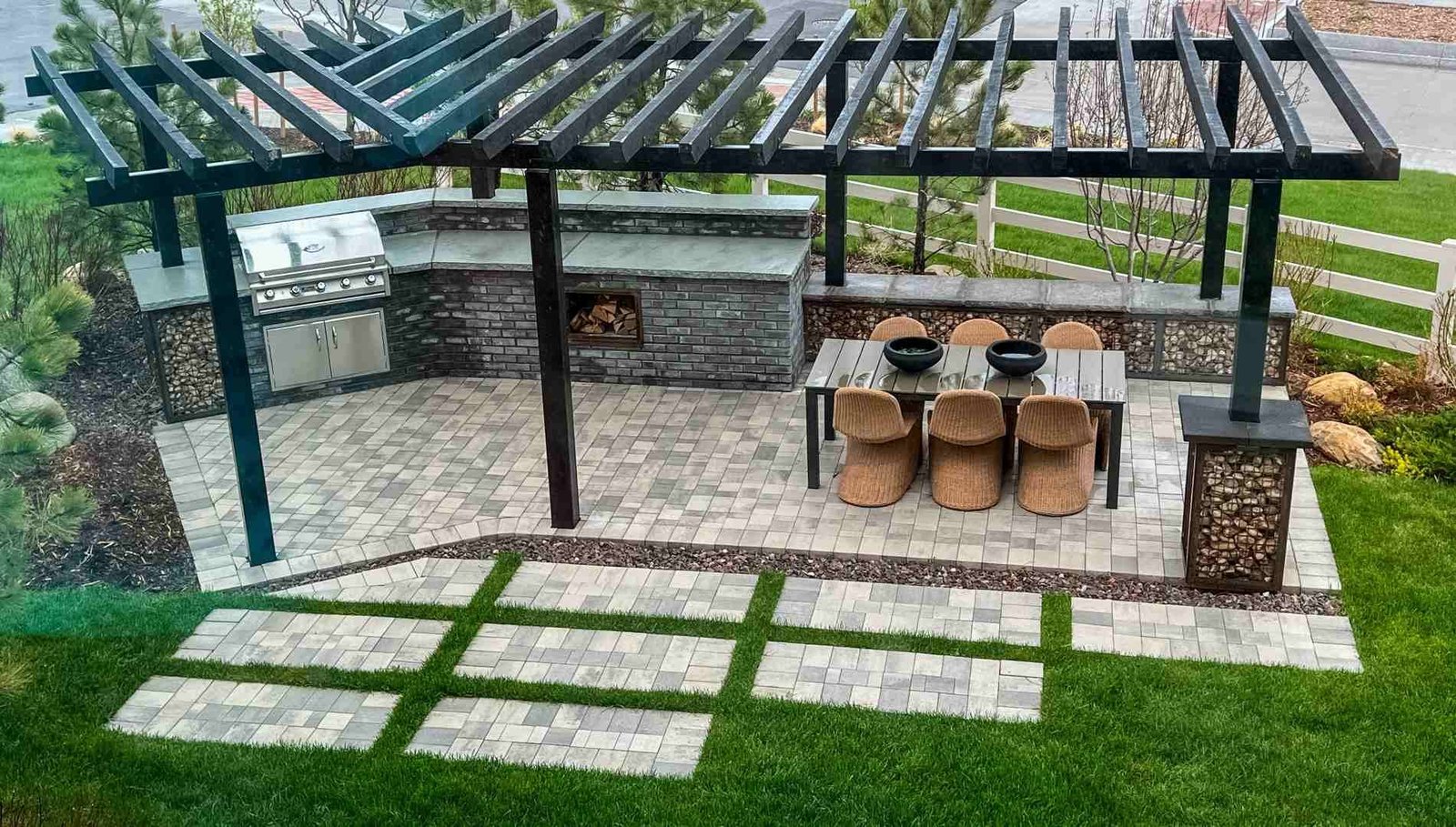 Backyard paver patio with a pergola, outdoor kitchen, and dining area, with paver stepping pads set into the lawn