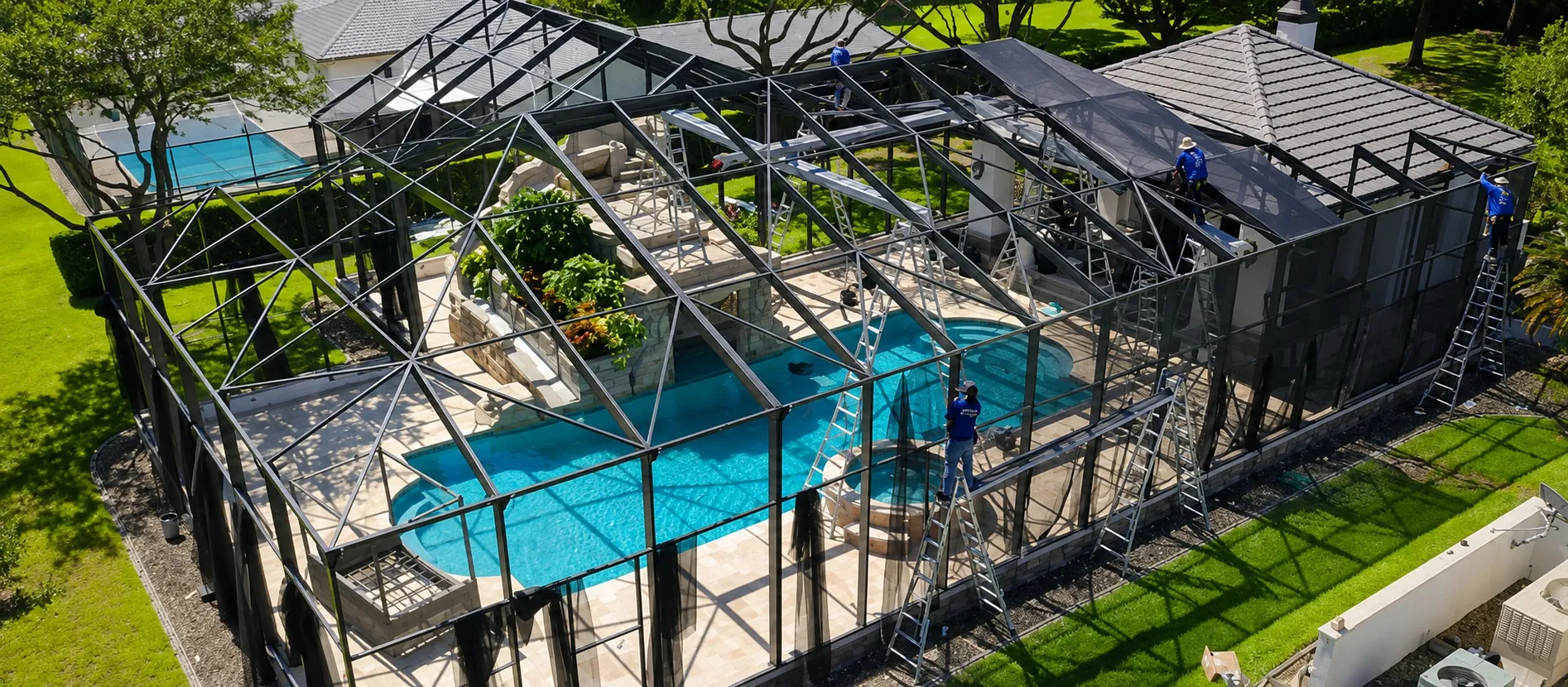 Pool cage mid-rescreen, the old panels stripped and the crew fitting new mesh