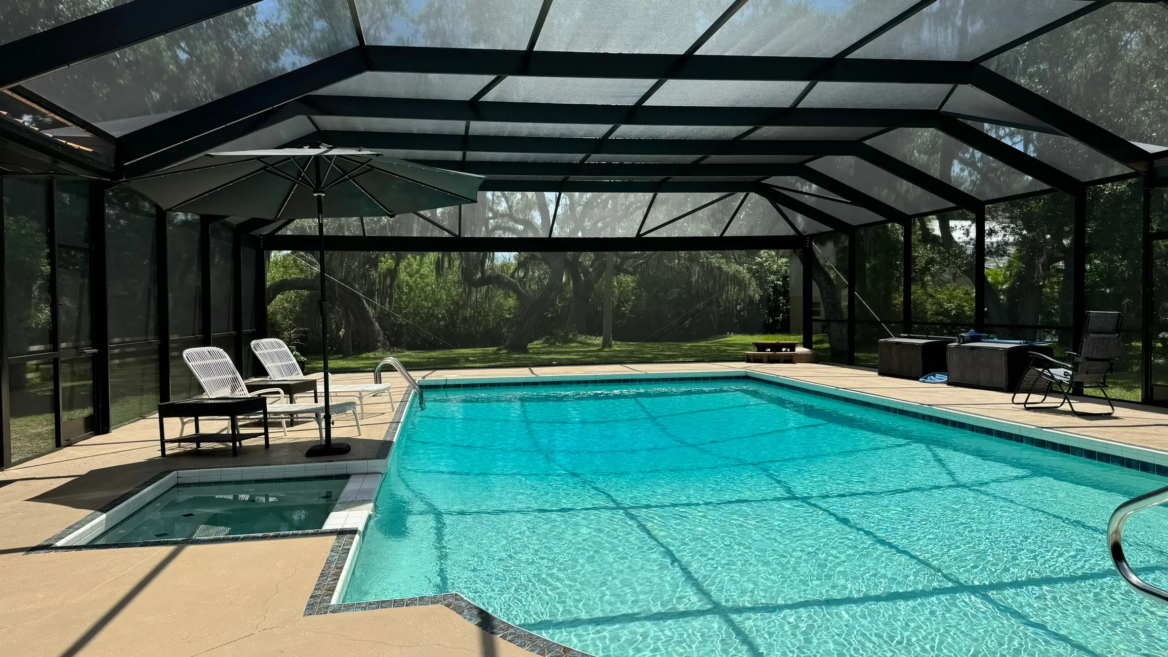 Restored pool cage seen from inside — dark aluminum frame, new screen panels and roof beams over the pool and spa
