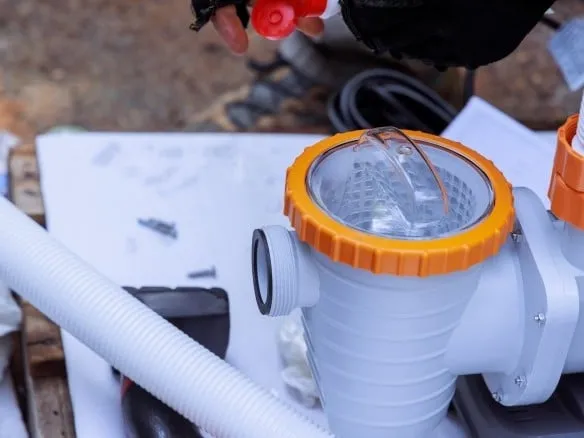 Technician assembling a pool pump strainer housing with orange lid ring and hoses during installation