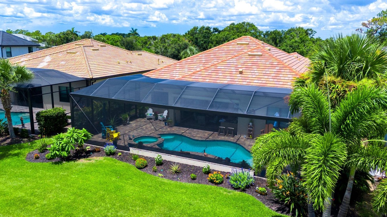 Aerial view of a black-screen pool enclosure over a freeform pool and spa at a tile-roof Florida home