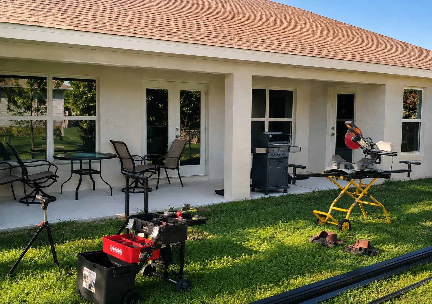 Covered patio with tools and aluminum profiles staged on the lawn before screen installation