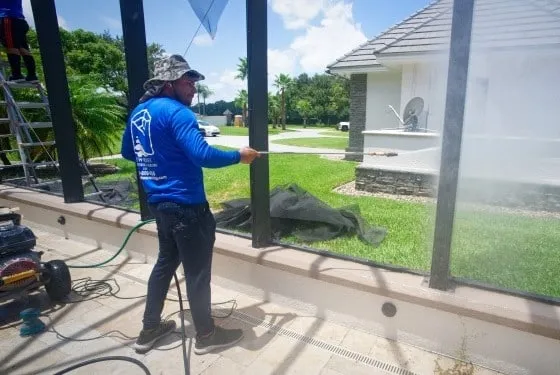 Technician pressure washing a pool cage frame with the screens removed