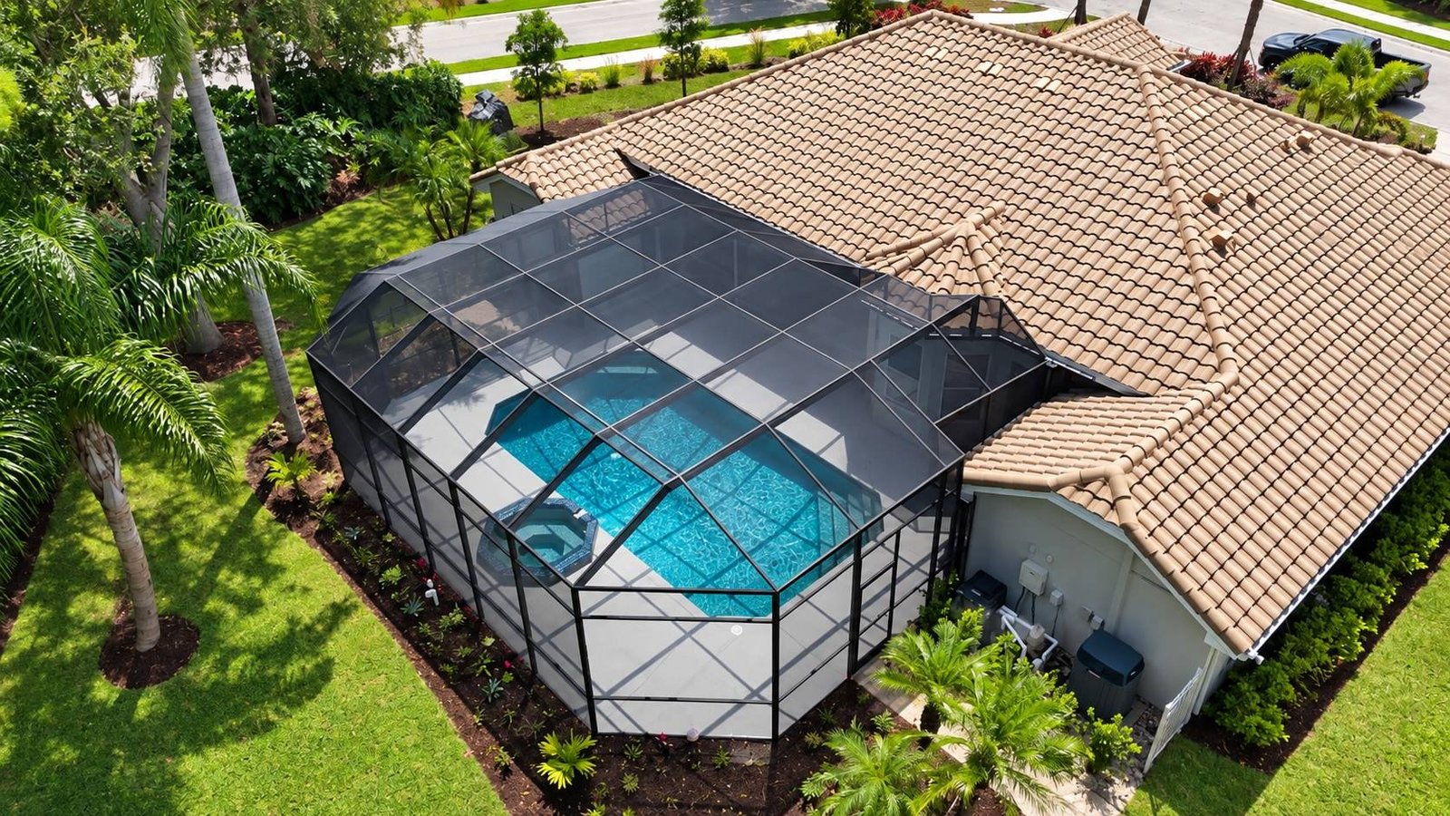 Aerial view of a freshly rescreened pool cage over a pool and spa at a tile-roofed Florida home
