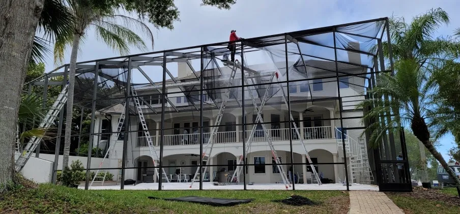Crew on ladders rescreening a tall pool cage on a three-story Sarasota home