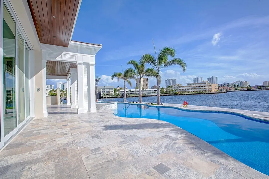 Silver travertine pavers in an ashlar pattern on a waterfront pool deck with palm trees