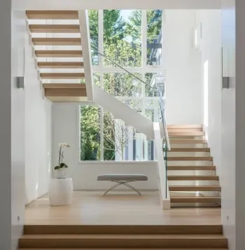 Switchback staircase with floating wood treads and glass railings by tall windows