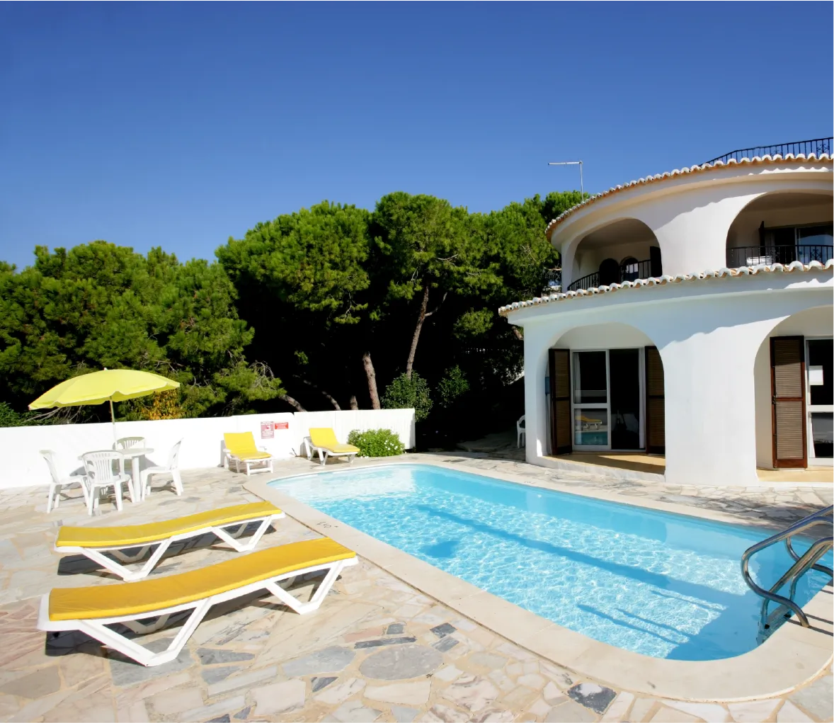 Natural stone pavers around a villa pool with yellow lounge chairs and an umbrella