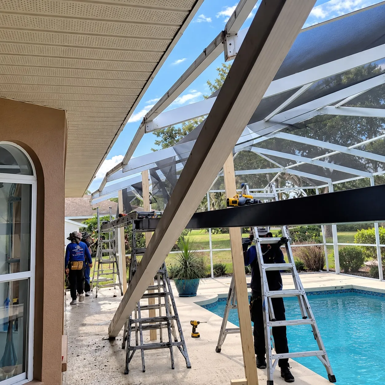 Crew shoring a pool cage roof with temporary posts while installing a new super gutter along the house fascia