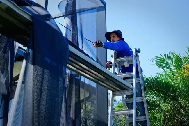 Technician on a ladder fitting new screen panels to a pool cage wall