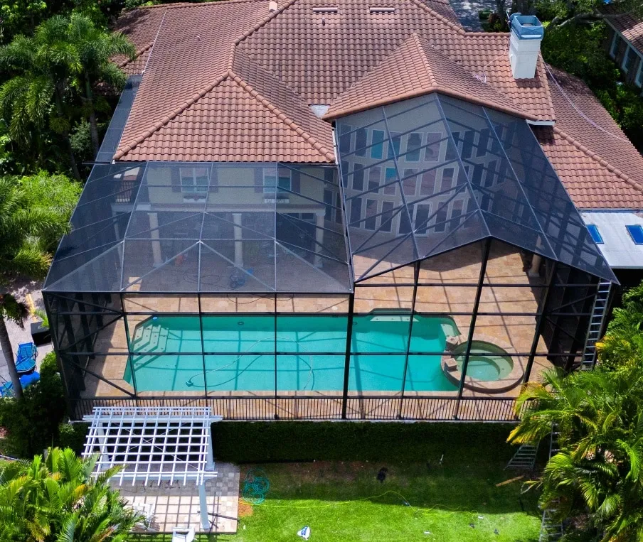 Aerial view of a screened pool cage over a tile-roofed Sarasota home