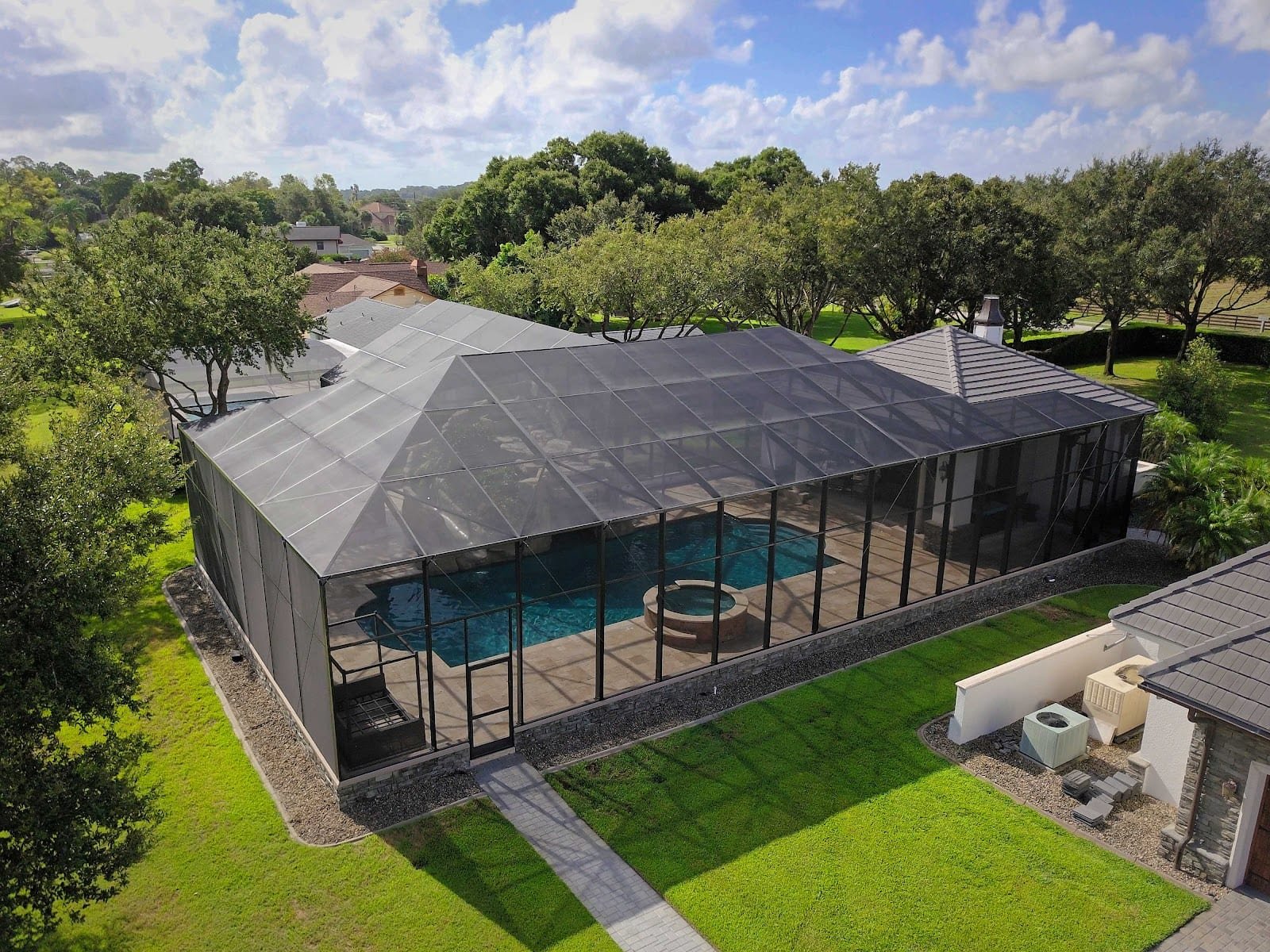 Aerial view of completed black aluminum pool cage enclosure with pool and spa inside, surrounded by landscaping.